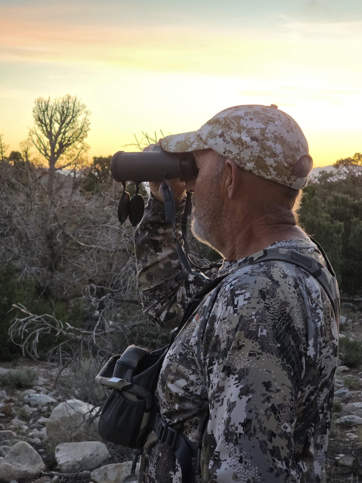 Hunter in camouflage using binoculars at sunset